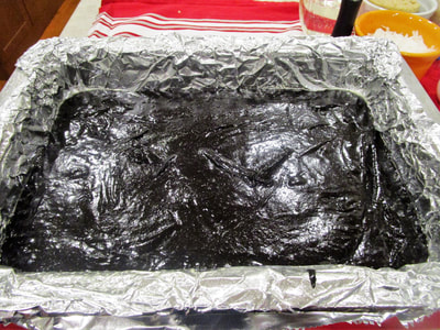 Brownie layer is ready to bake in a foil-lined pan